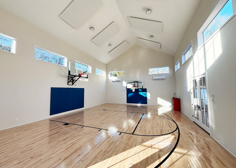 Bright and Indoor basketball court with windows, wooden floor and white walls, featuring two basketball hoops and acoustic panels on walls.