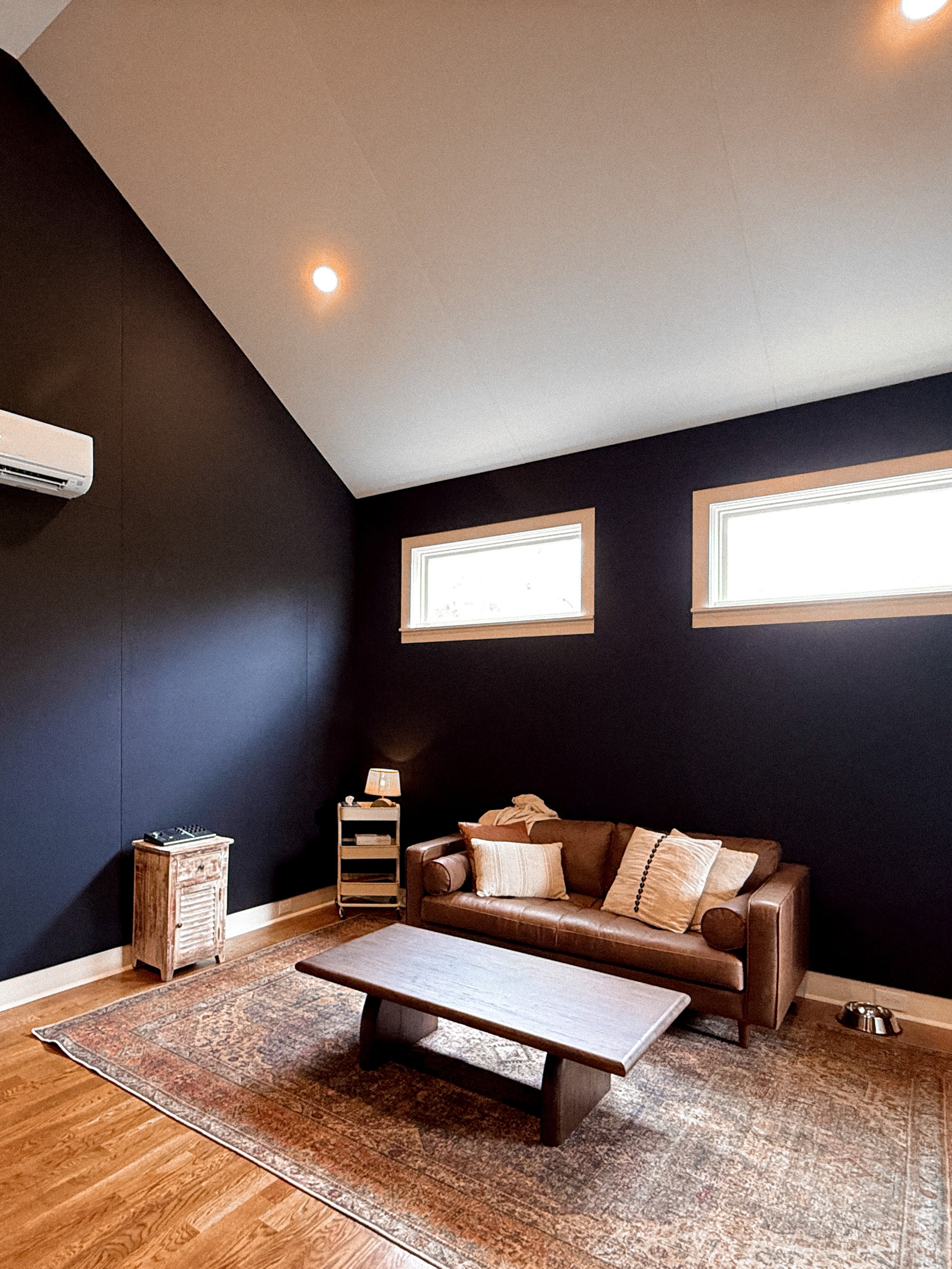 Modern living room with dark blue fabric track acoustic treatment walls, brown sofa, and wooden coffee table.