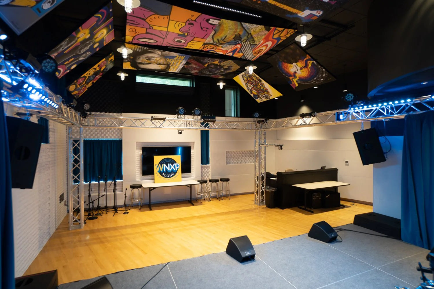 Modern studio with colorful ceiling art, WNXP logo on screen, and audio equipment.