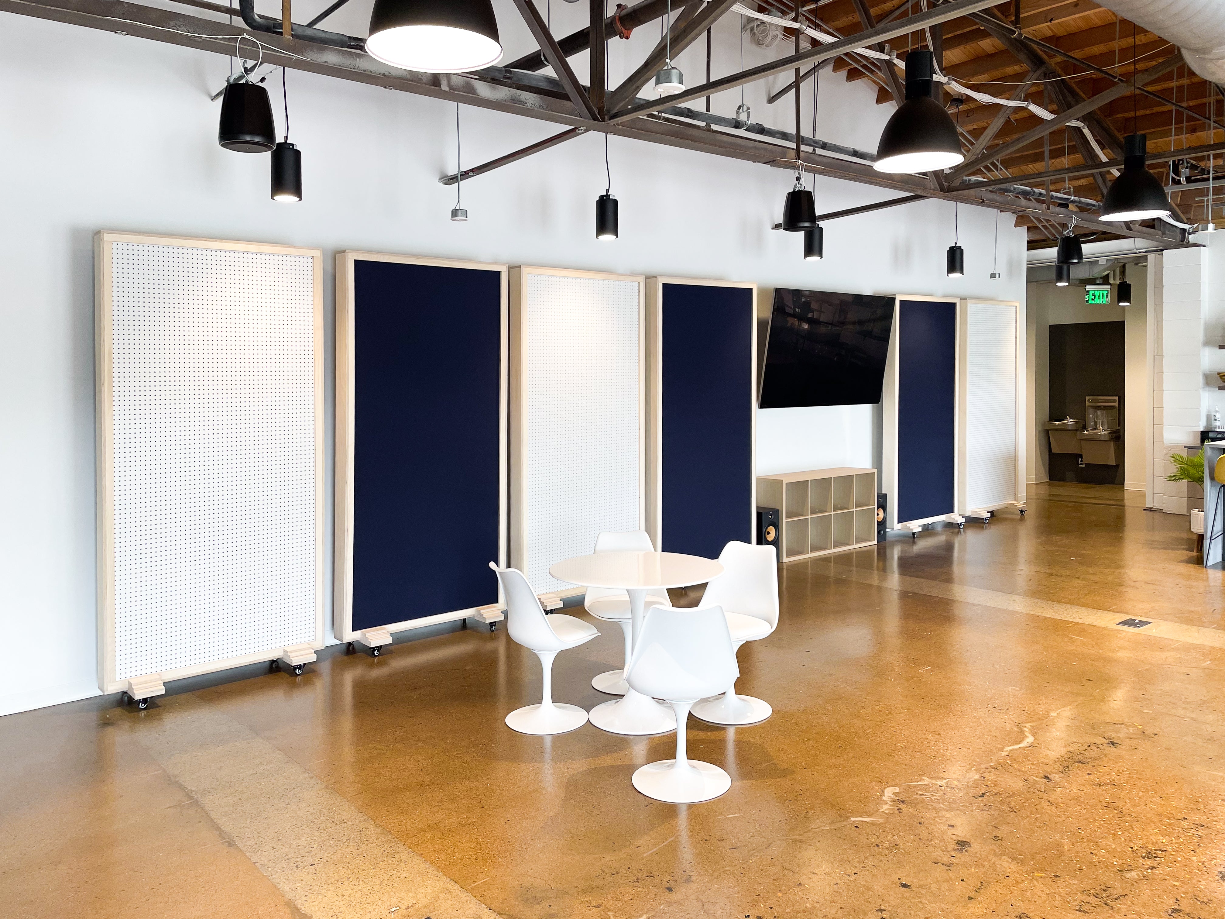 Modern office space with white chairs and tables on a polished wooden floor. Music City Acoustics Gobos line the wall. 