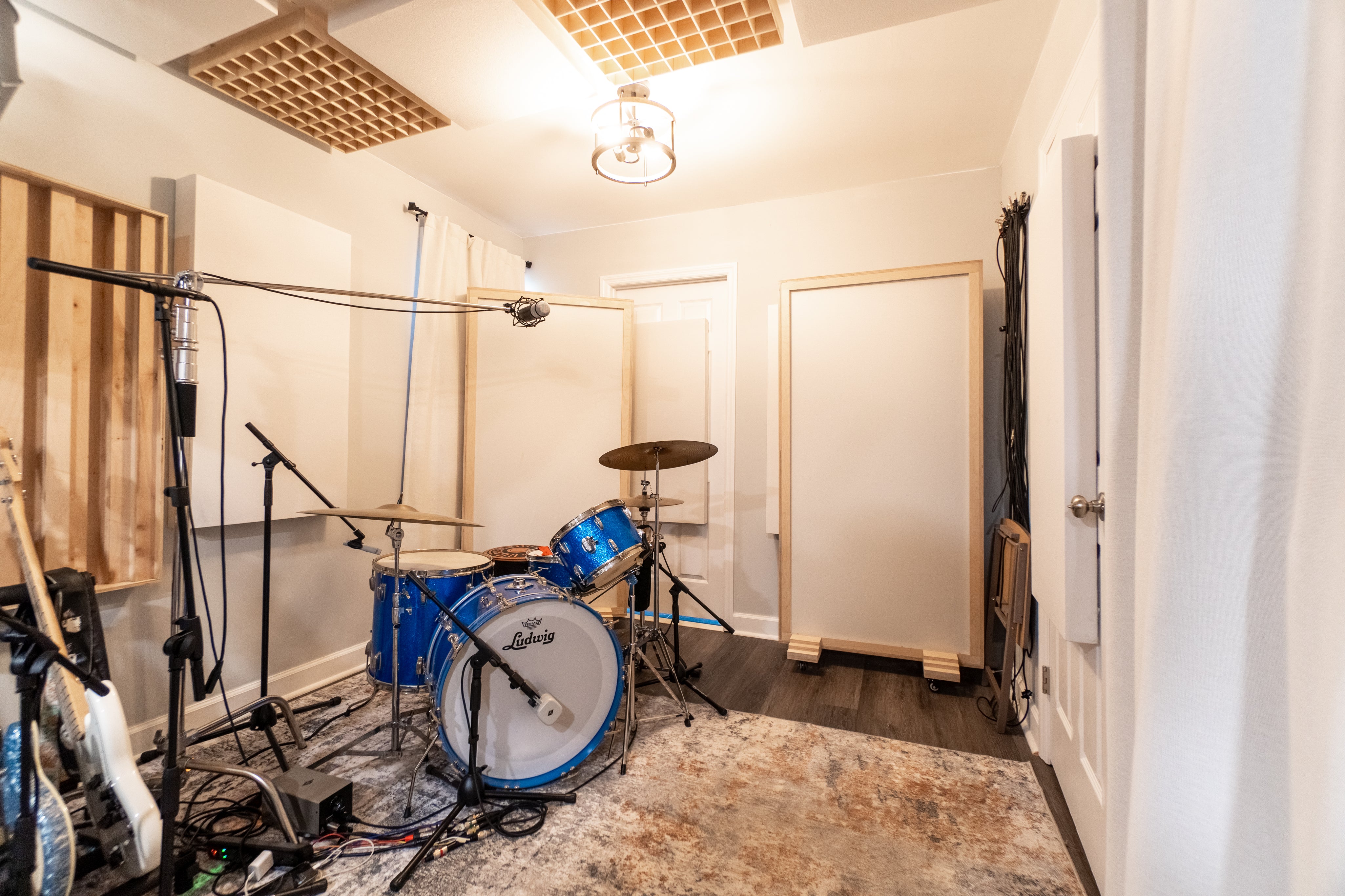 home Music studio with a drum set, guitars, Music City Acoustics gobos and diffusers and microphones on a carpeted floor.