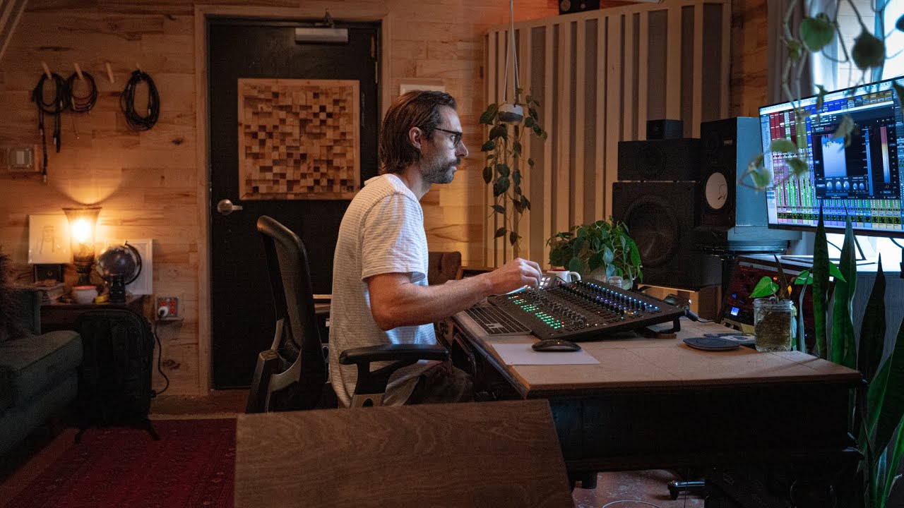 Man working at a music production desk with multiple screens in a home studio.