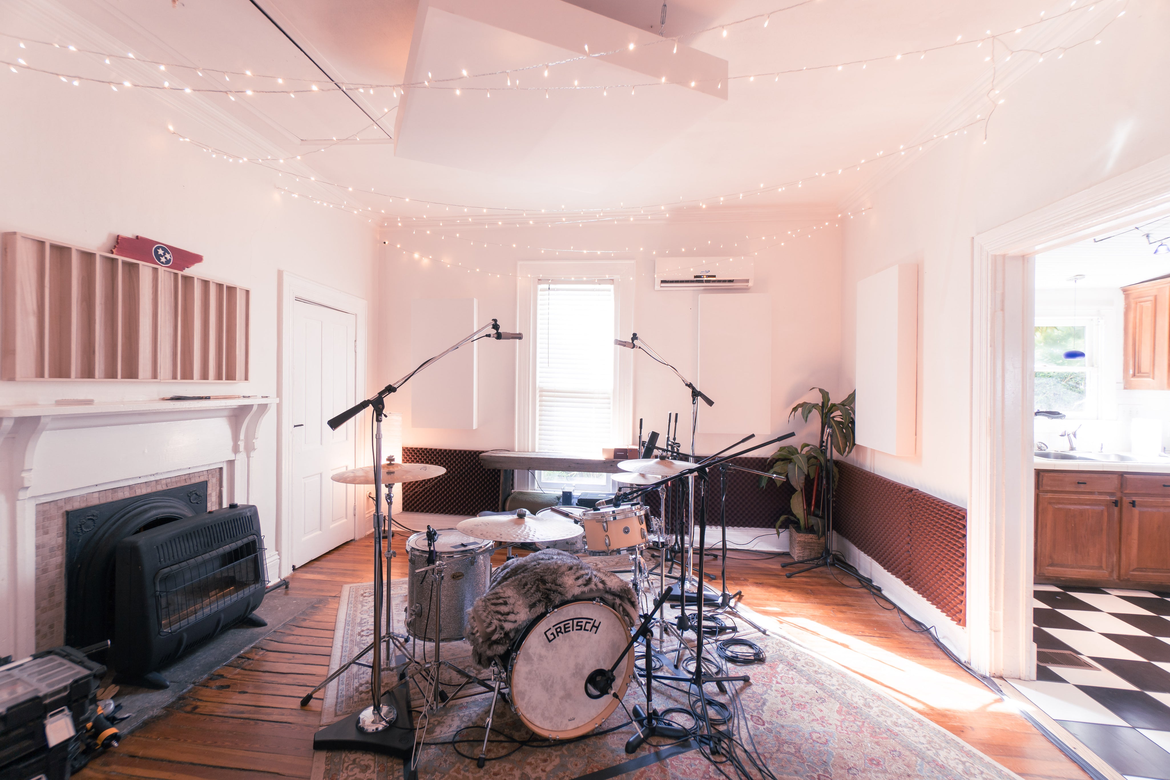 Music studio with drum set, microphones, and equipment on a wooden floor.